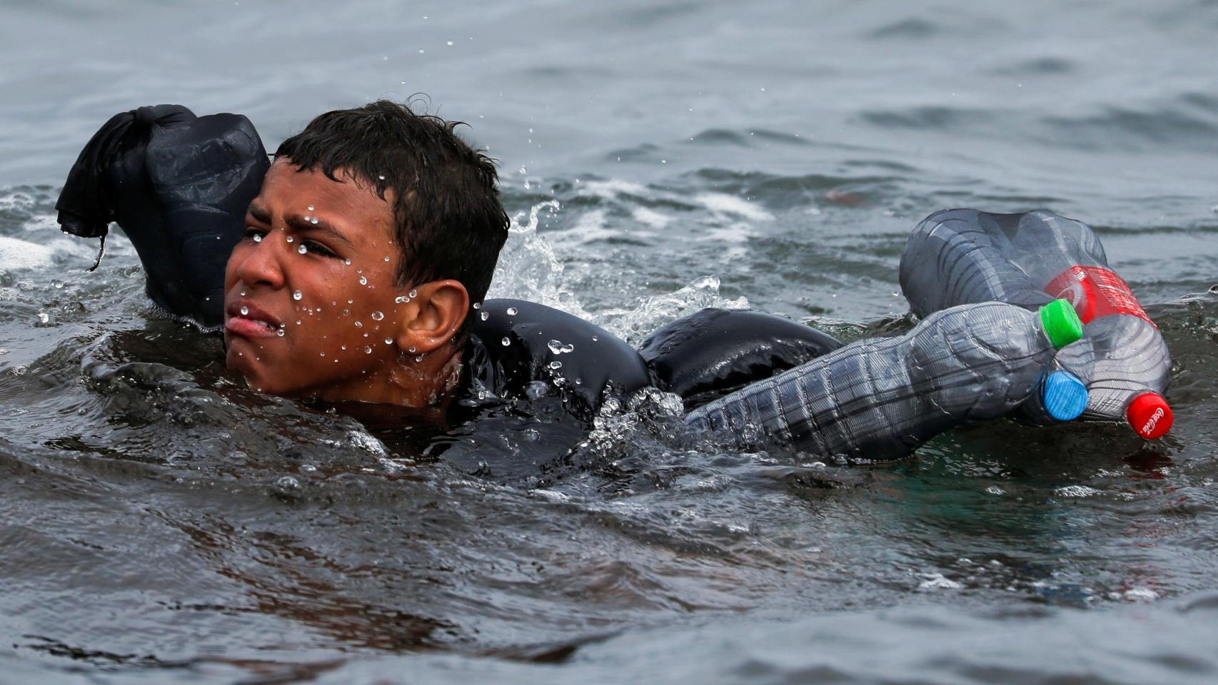 Un menor marroquí trata de alcanzar la playa de Ceuta.
