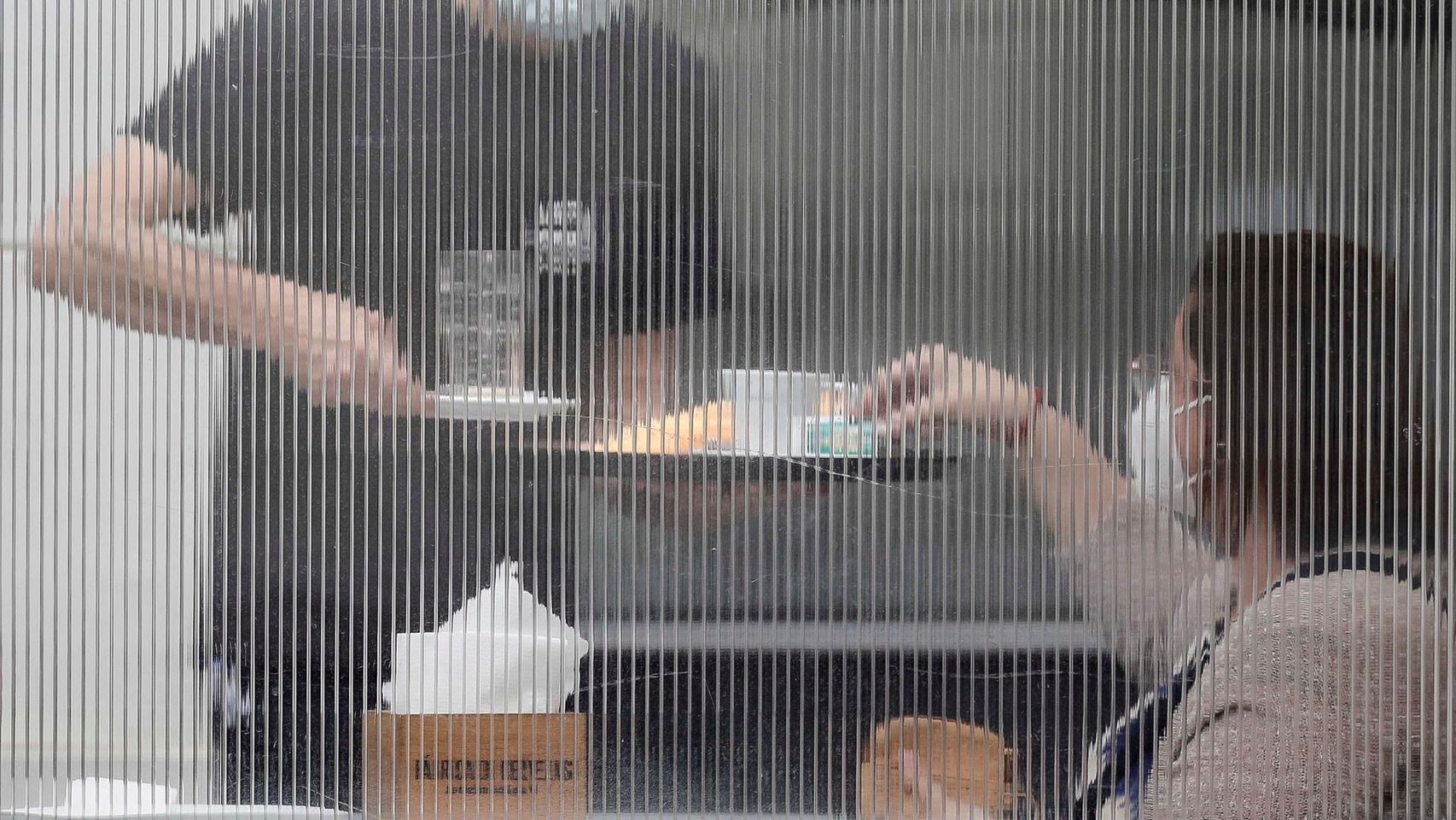 Un camarero sirve a una mesa tras una mampara.