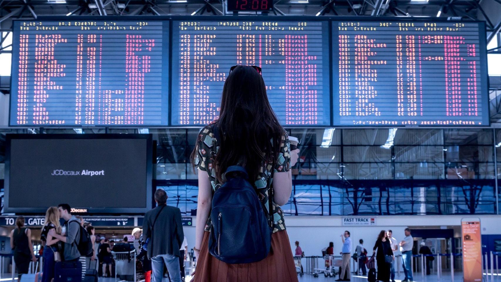 Una turista frente al panel de destinos de un aeropuerto.