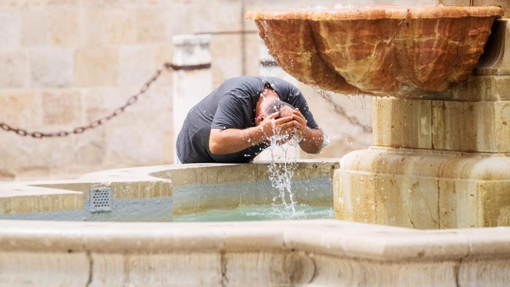 Una persona refrescándose en una fuente.