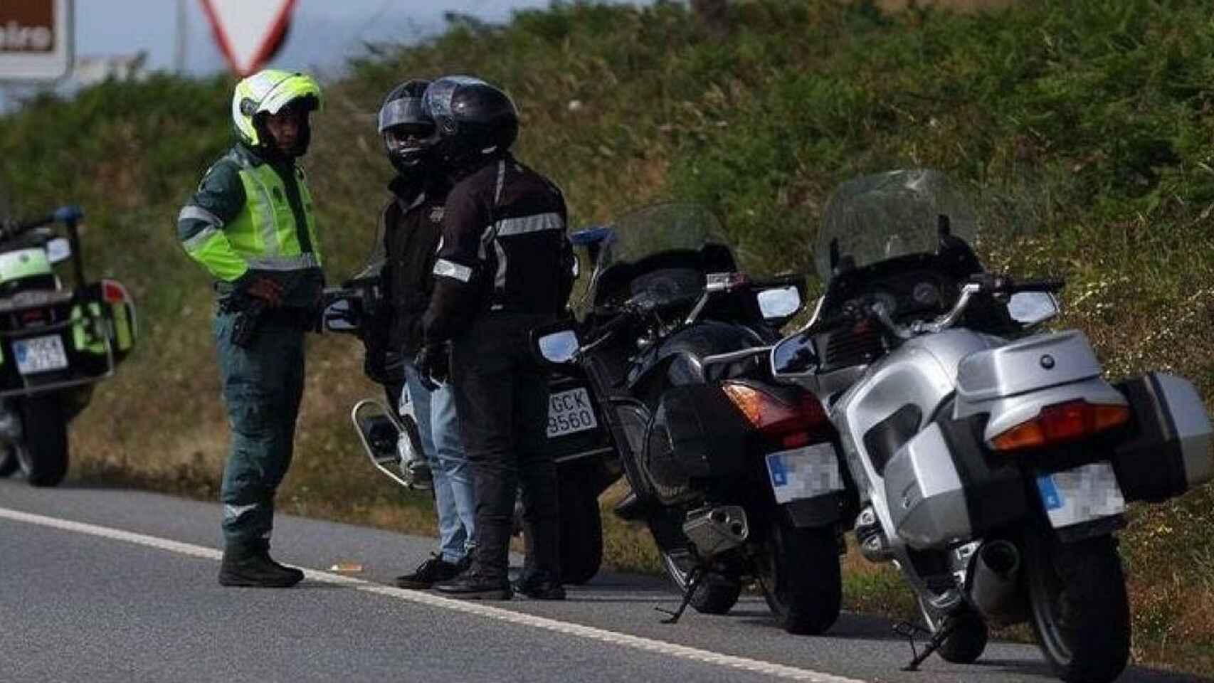 Un agente de la Guardia Civil dialoga con dos motoristas en la carretera.