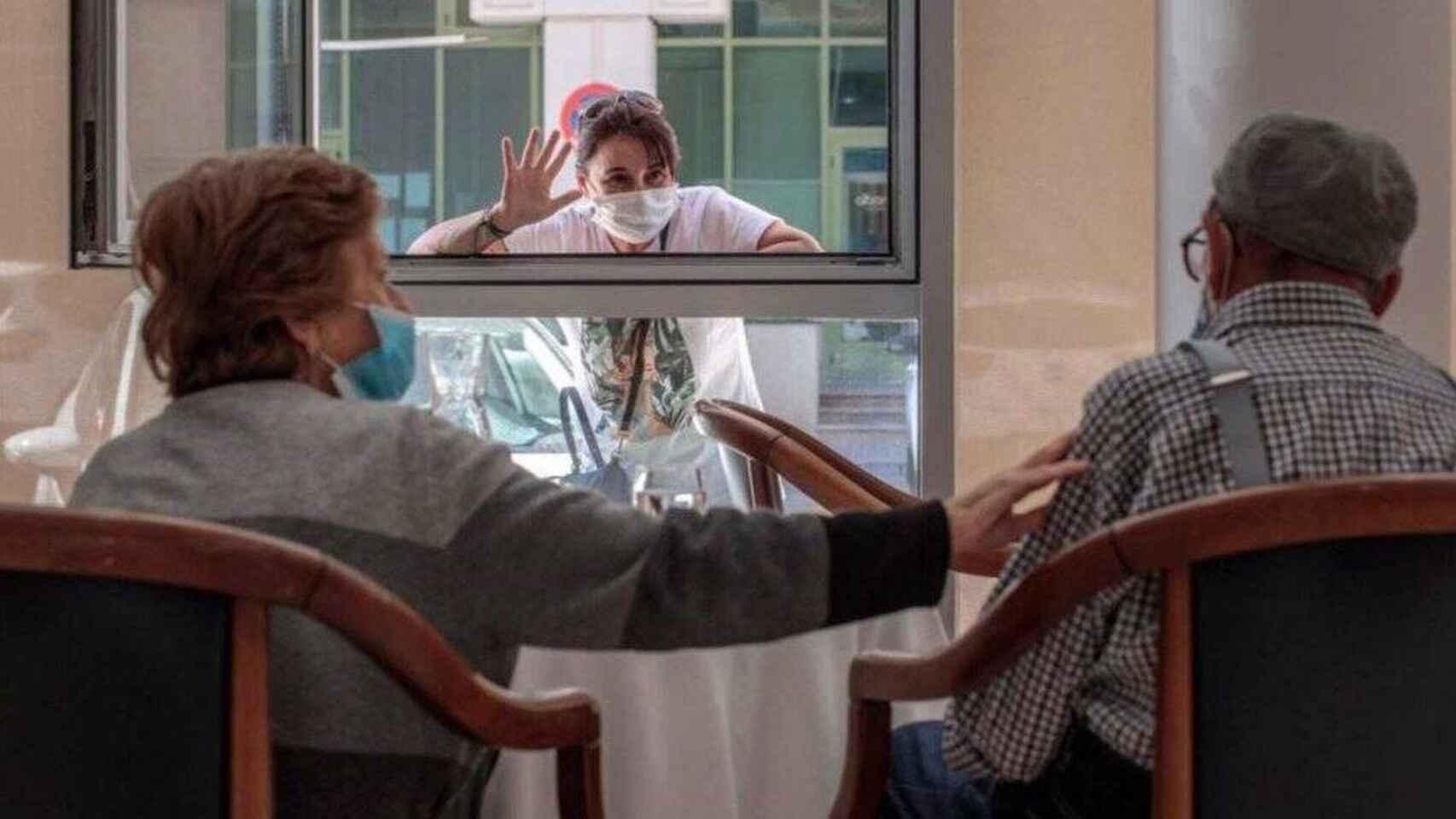 Dos personas mayores son saludadas desde el exterior de una residencia.