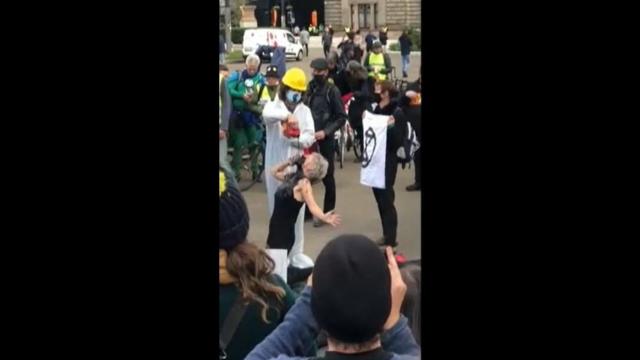 El momento en que la manifestante simula beber petróleo.