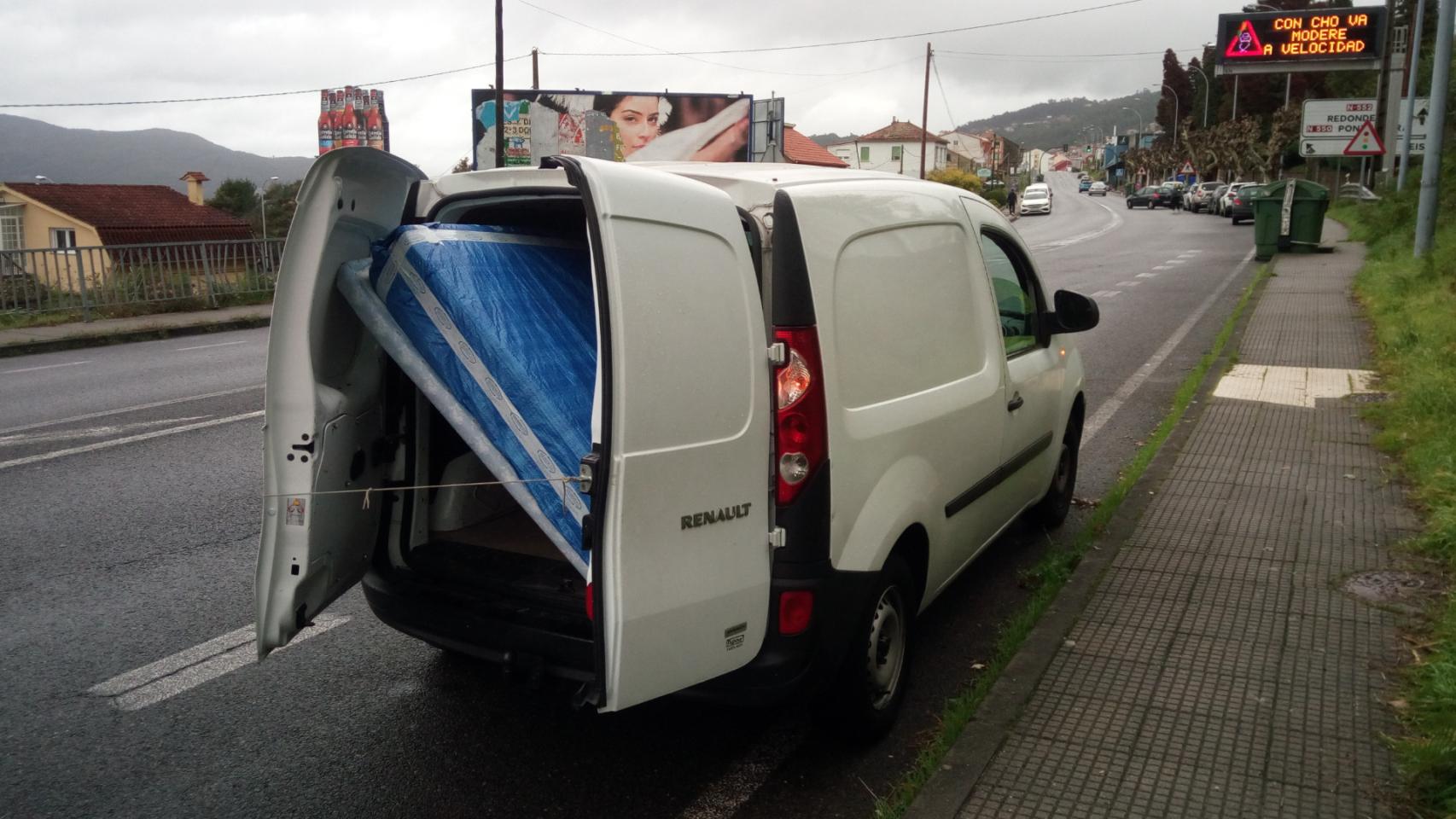 Furgoneta con los portones abiertos y un colchón y un canapé como carga.