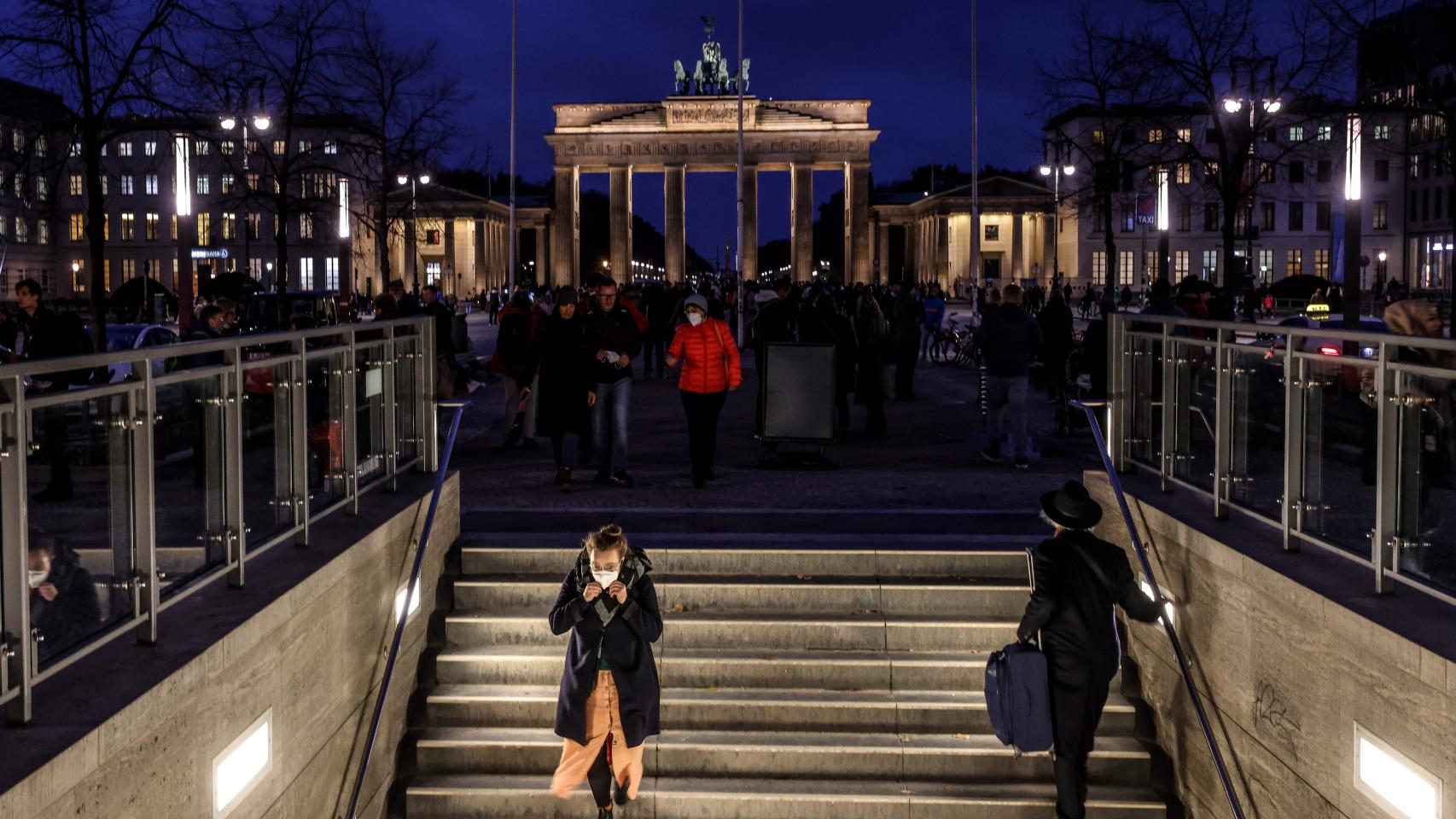 Transeúntes en una boca de metro en Berlín, con la puerta de Brandeburgo al fondo.