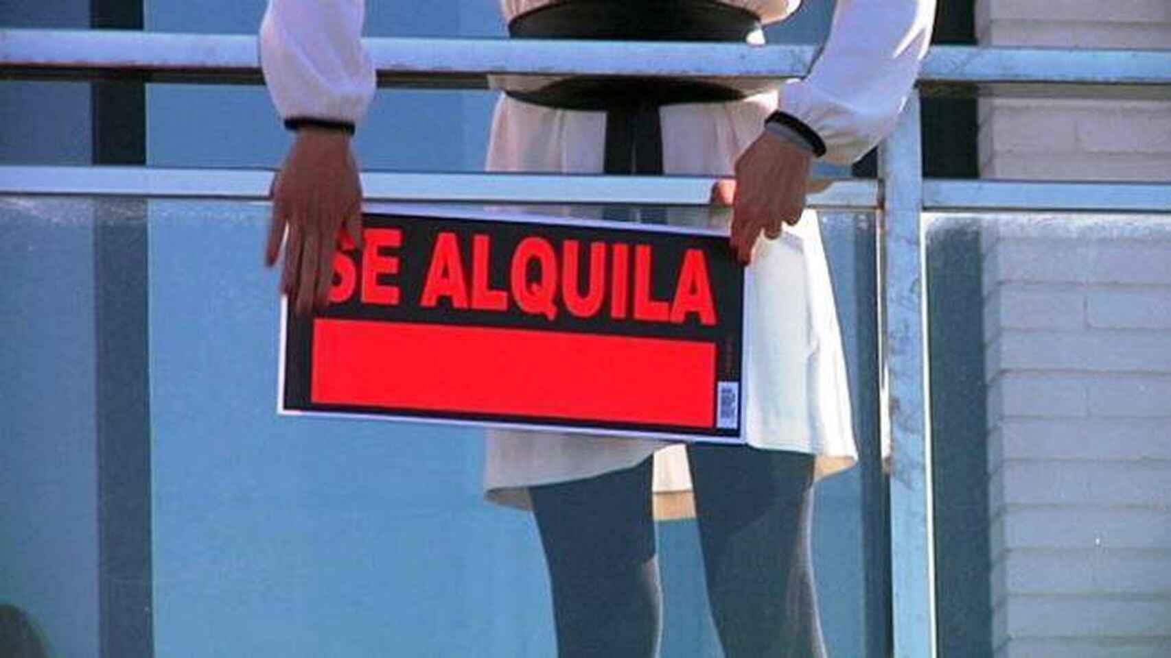 Una mujer cuelga el cartel de se alquila en una vivienda
