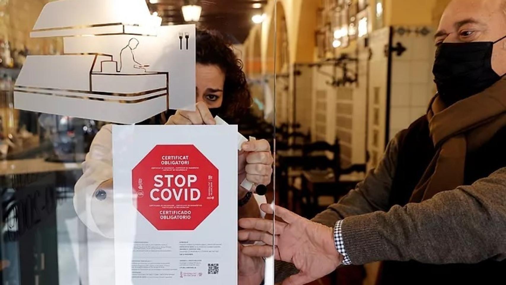 Un local colgando un cartel sobre la obligatoriedad del certificado Covid.