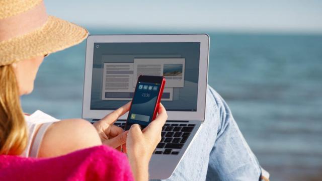 Una mujer con su móvil y su portátil en la playa