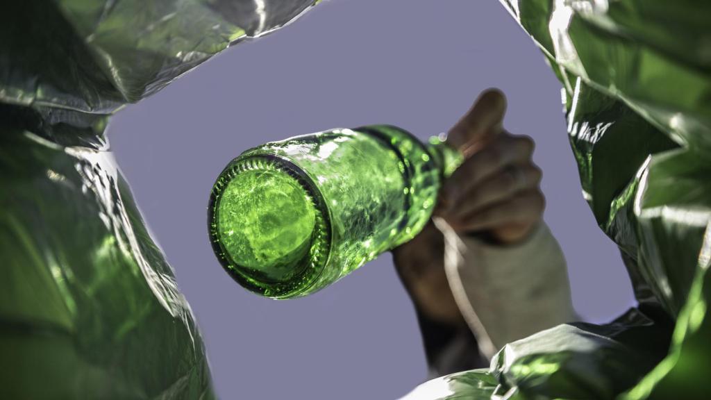 Una mujer tira una botella en un cubo de basura