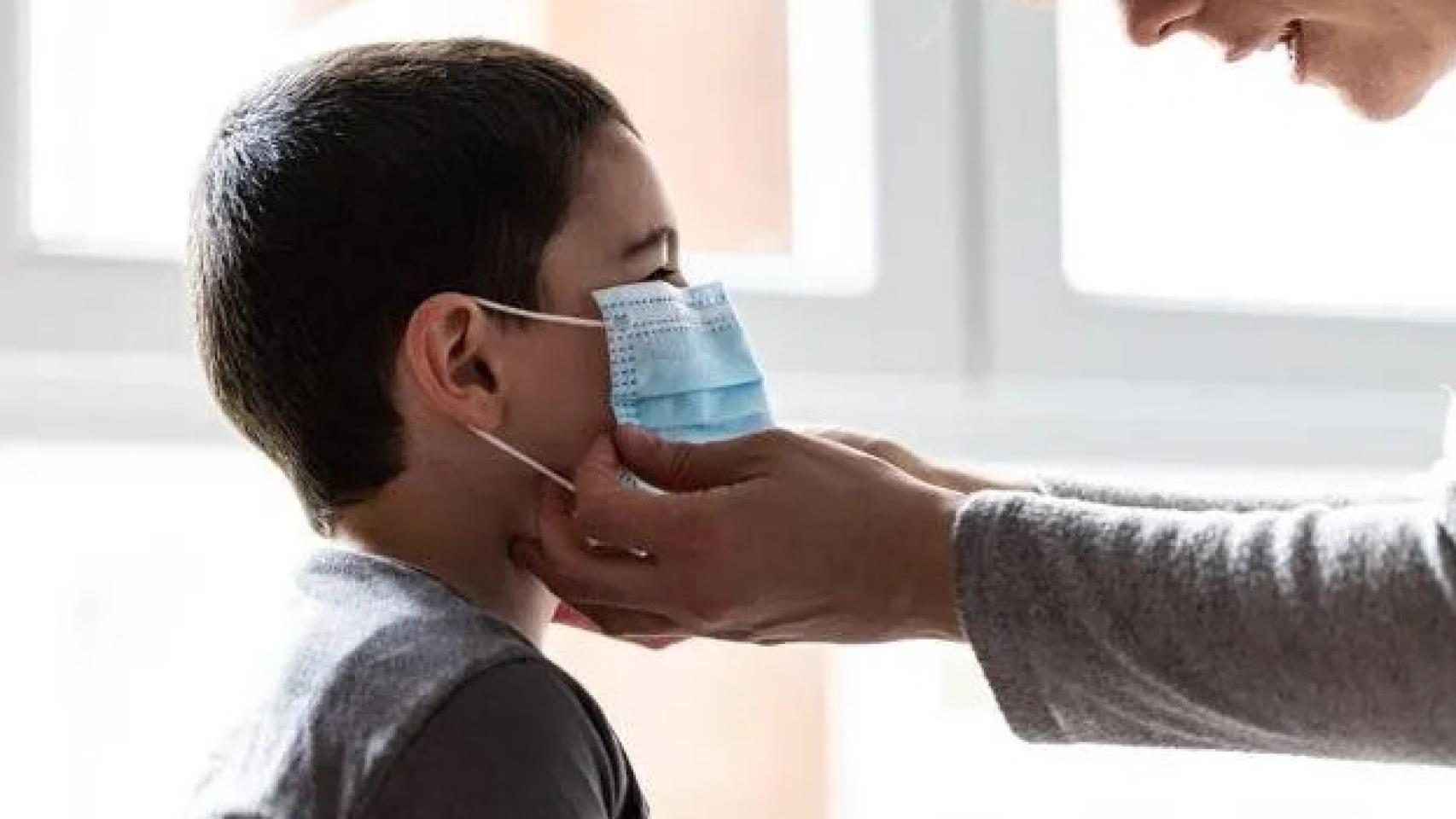 Una madre coloca a su hijo una mascarilla.