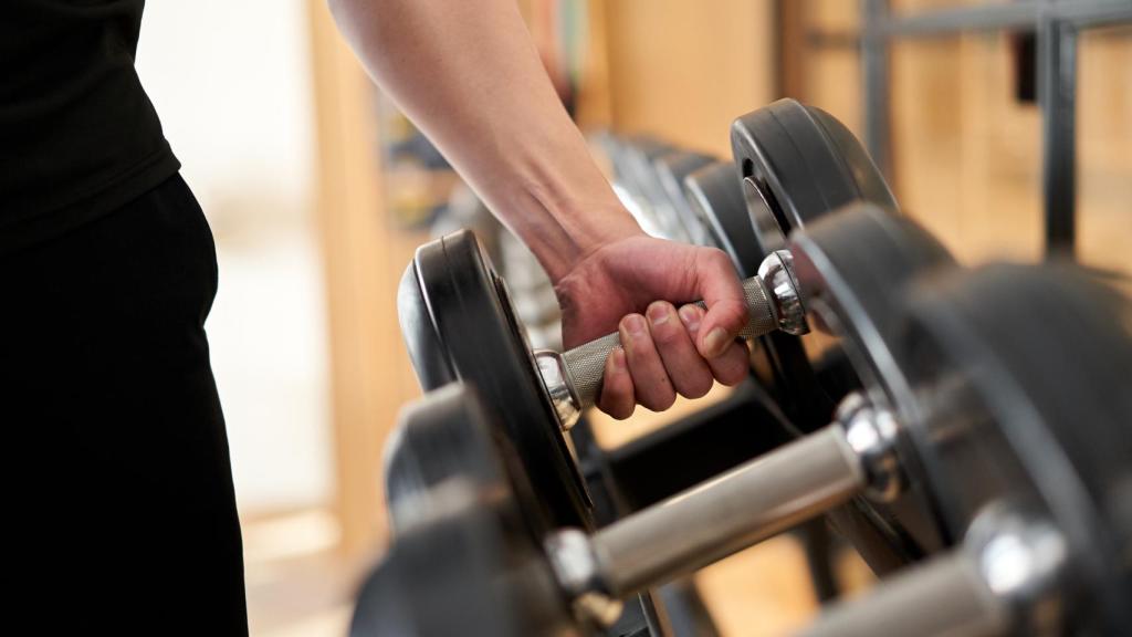 Una persona intenta coger unas pesas en el gimnasio.