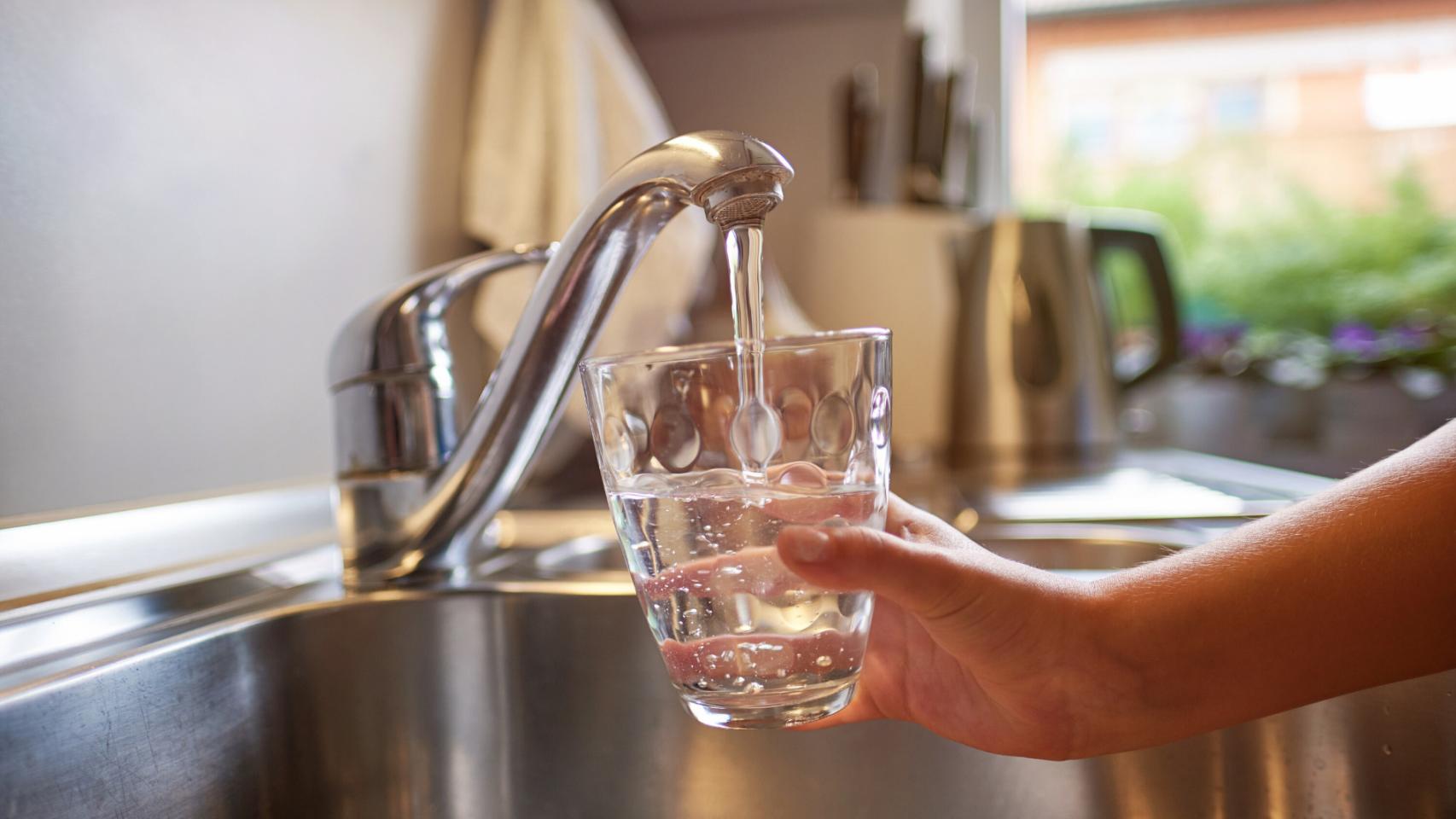 Un hombre bebe un vaso de agua del grifo.