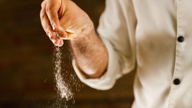 Un cocinero echando sal a alguna comida.