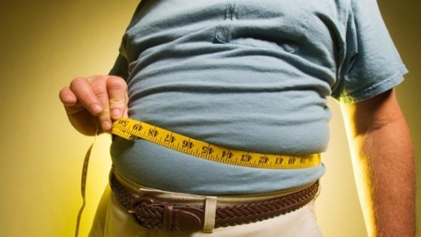 Un señor mide su barriga con una cinta métrica.