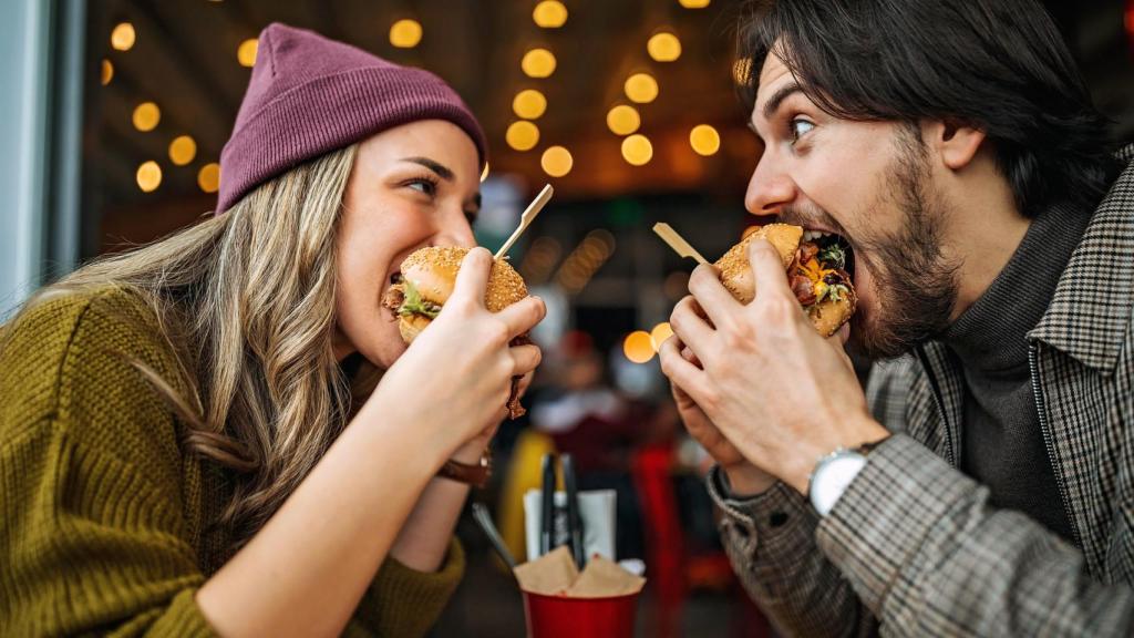 Dos jóvenes comiéndose una hamburguesa.