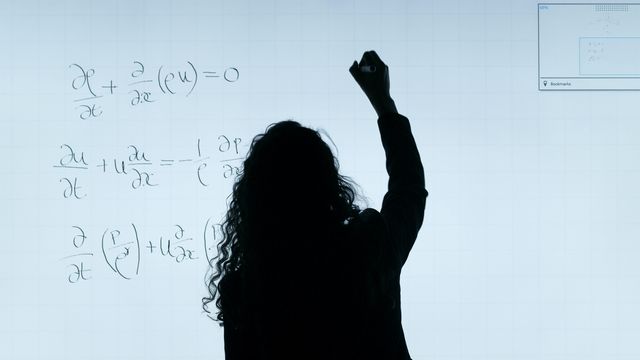 Una mujer escribe operaciones matemáticas en una pizarra.
