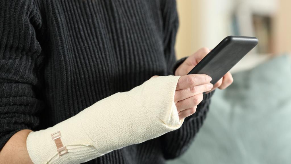 Una mujer con la muñeca lesionada consulta su teléfono móvil.