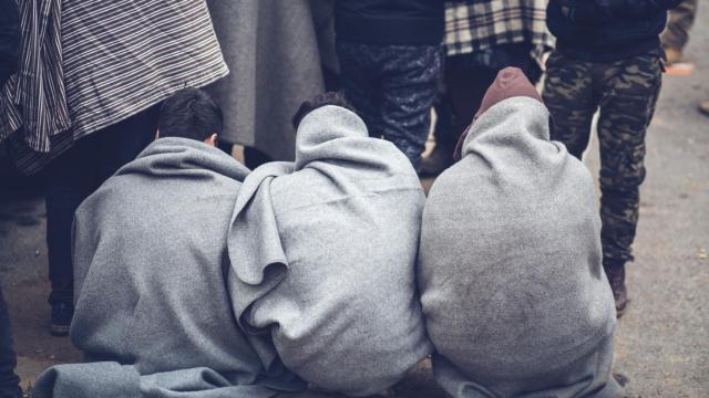 Un grupo de migrantes sentados y de espaldas a cámara