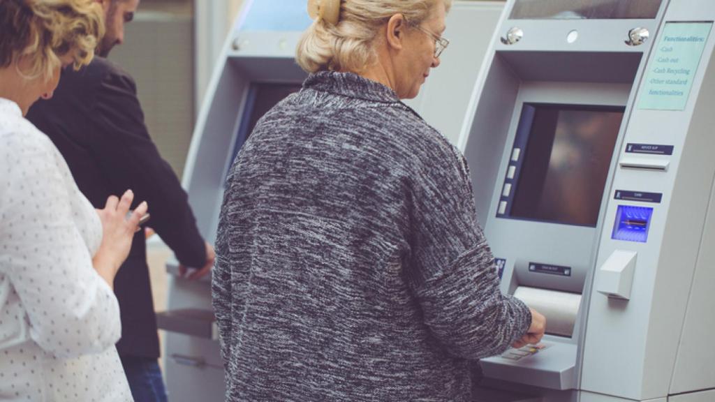 Una jubilada retira dinero de un cajero.