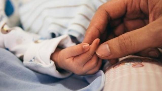 Un bebé  y una mano de un adulto.
