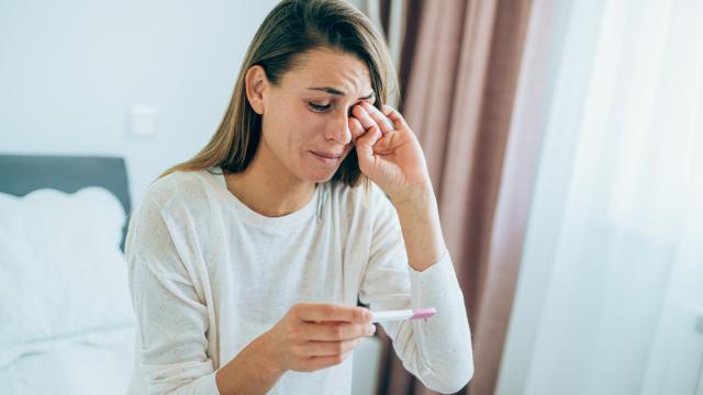 Mujer joven triste con prueba de embarazo en casa.