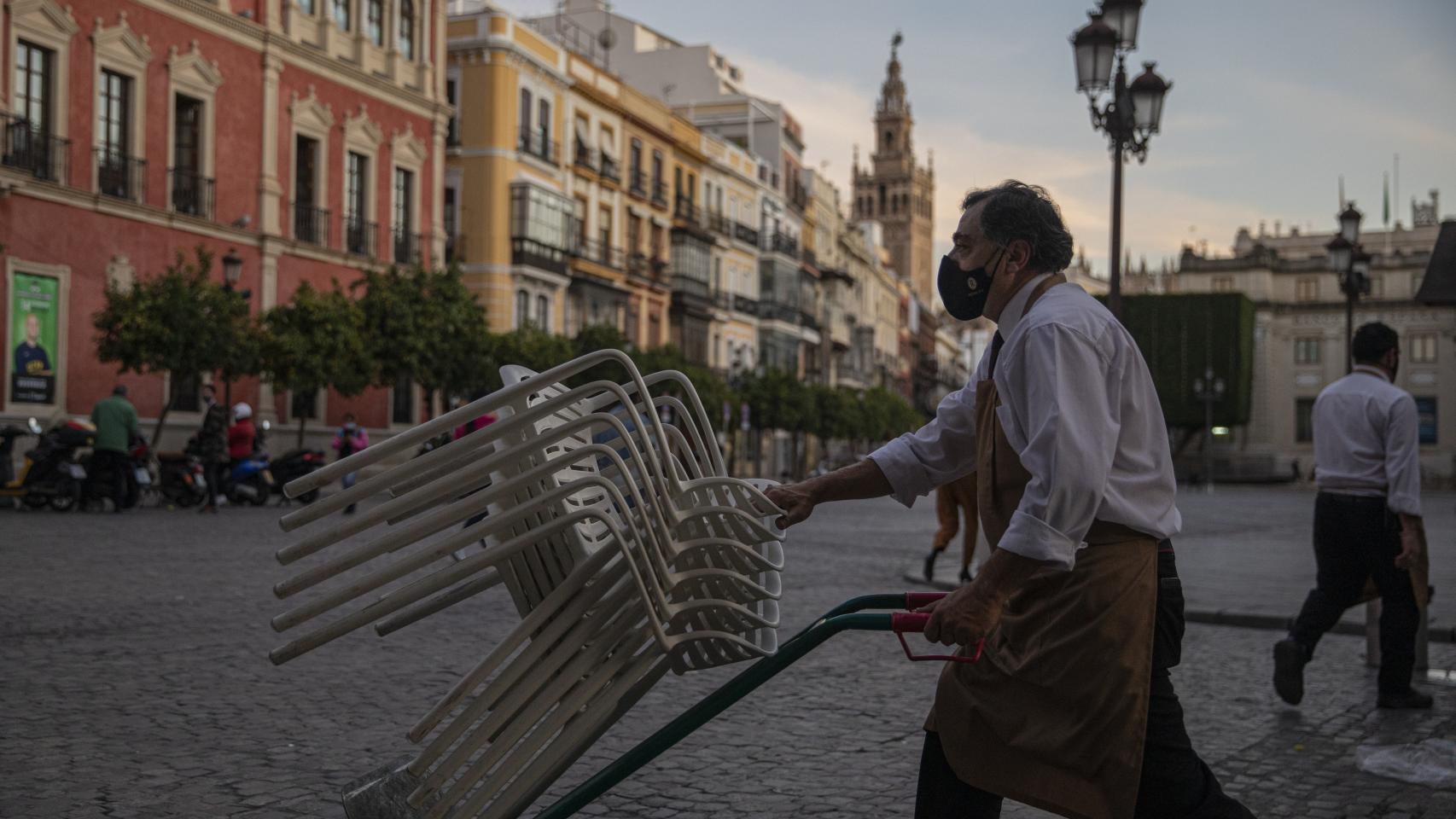 Un camarero recoge el mobiliario de un bar en Sevilla.