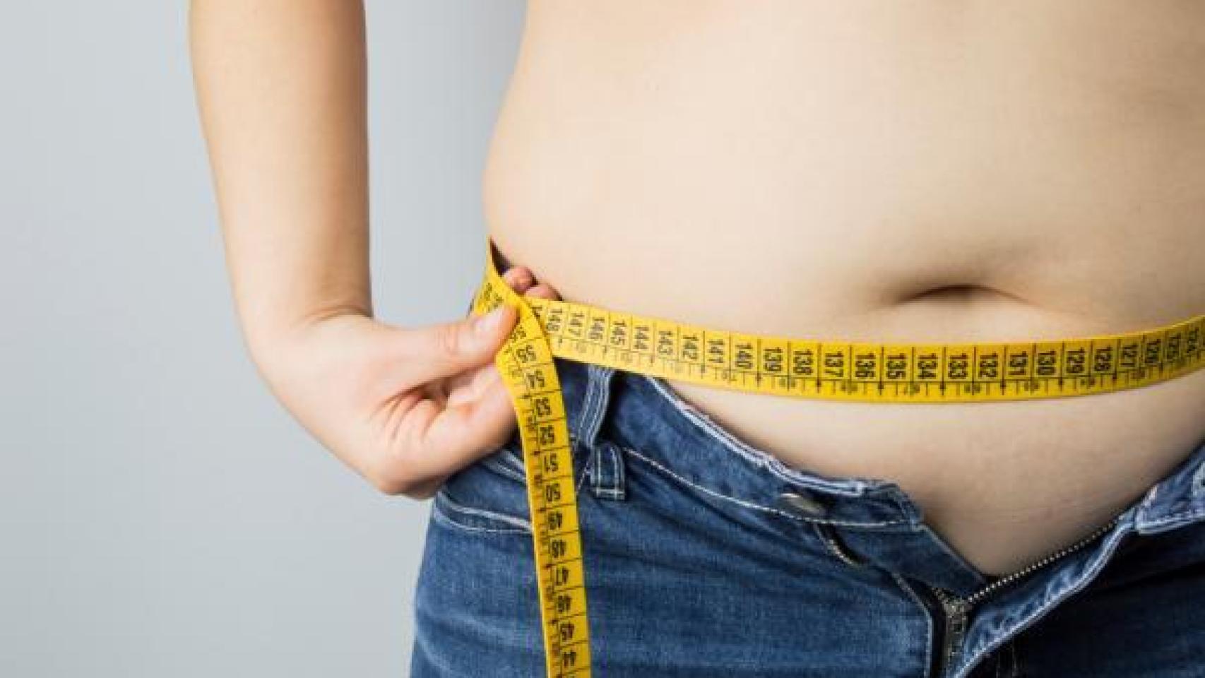 Un joven se mide la barriga con una cinta métrica.