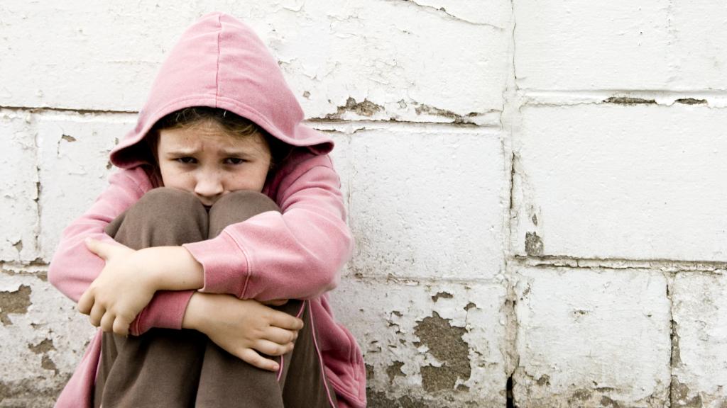 Imagen de archivo de una niña sentada en el suelo con aspecto triste.