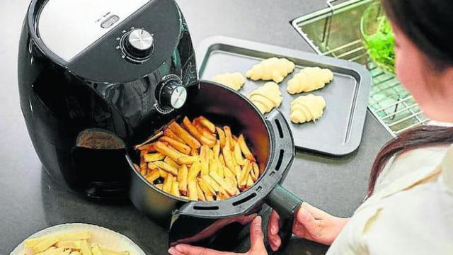 Una persona haciendo patatas en la freidora de aire caliente.
