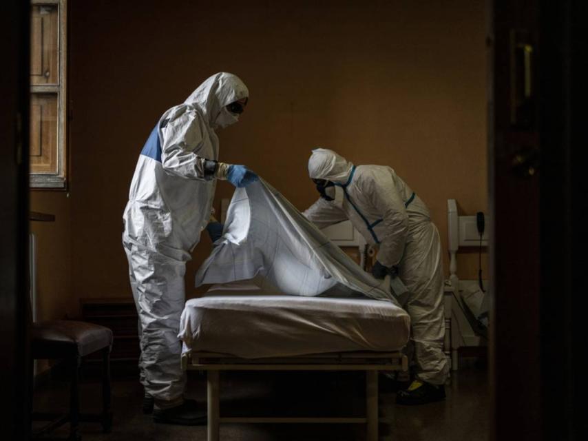 Dos trabajadores con EPI desinfectan una cama en una residencia de ancianos.