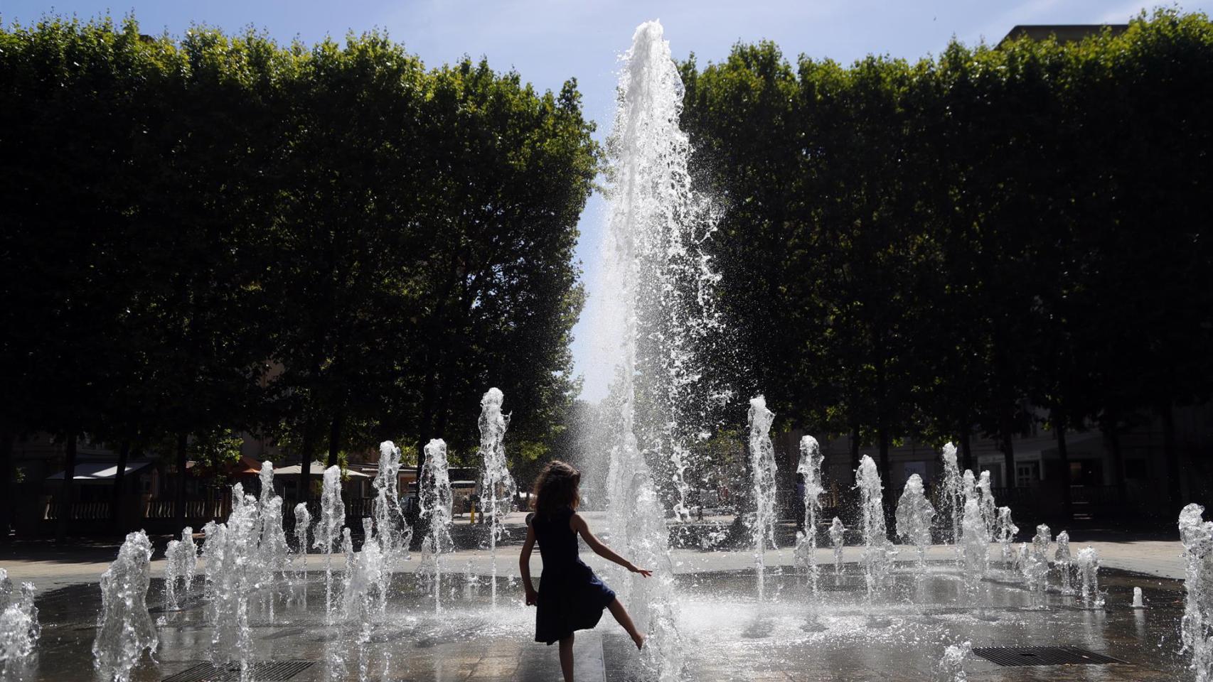 Una niña se refresca en una fuente.
