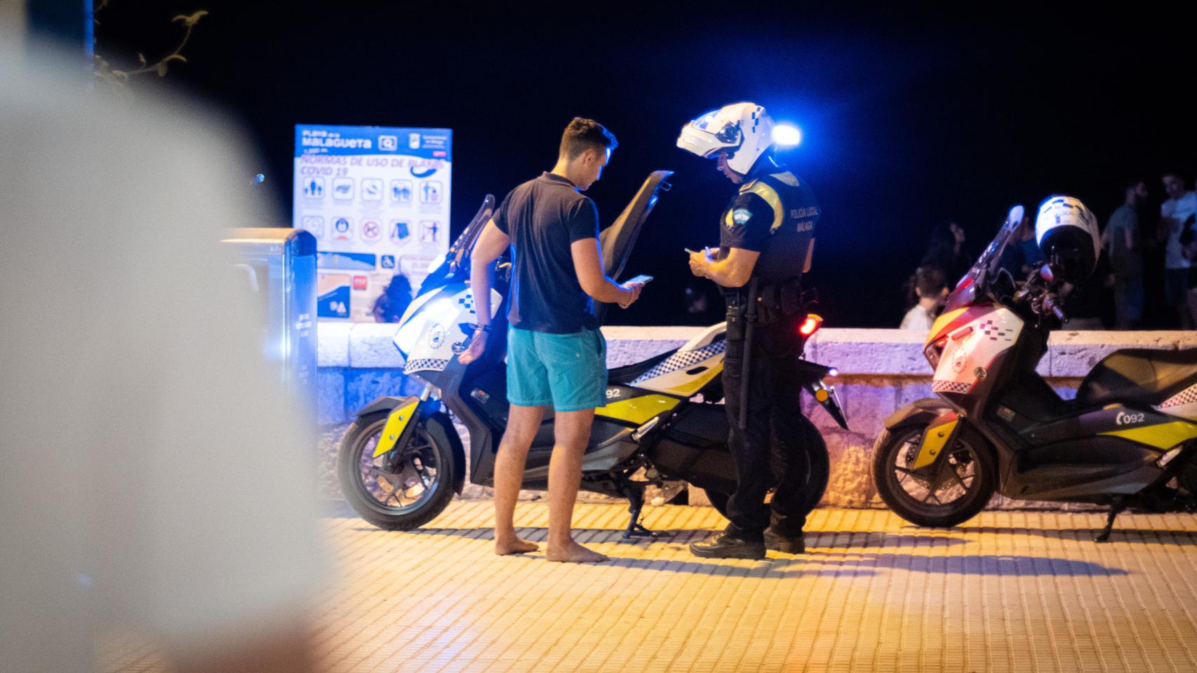 Un policía para a un joven en la noche de San Juan en Málaga.