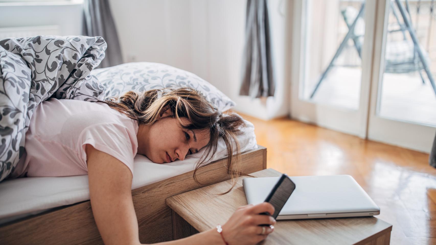 Una mujer mira el móvil desde la cama.