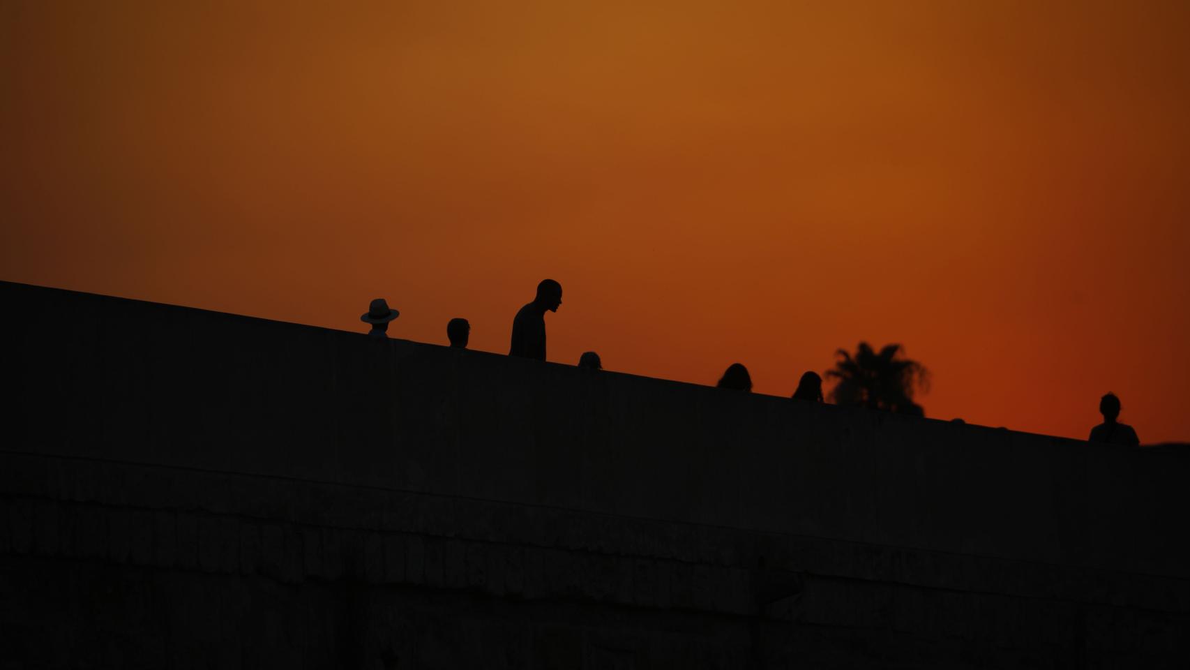 Varias personas pasean por el puente romano de Córdoba al atardecer en una jornada donde continua la ola de calor con temperaturas que alcanzan los 43 grados.