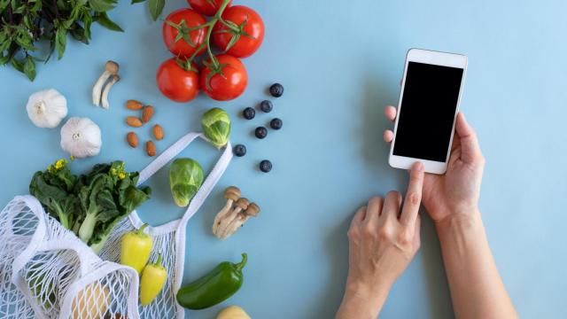 Una persona con un teléfono móvil junto a verduras y hortalizas.