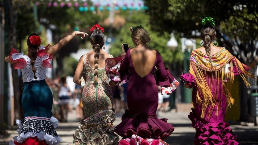 Cuatro personas vestidas de flamenca en la Feria de Málaga, una de ellas con mantón.