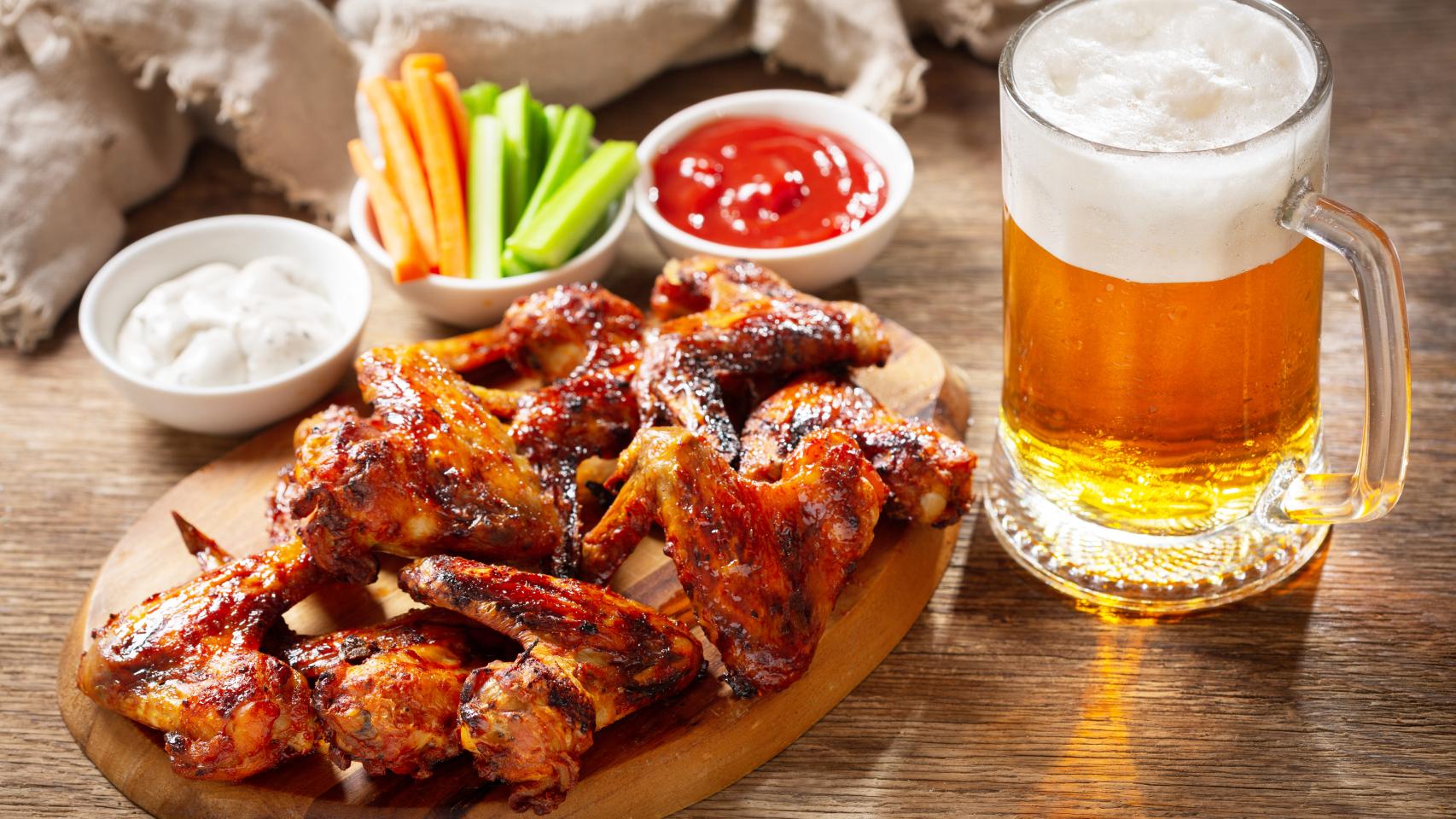 Una cerveza con alitas de pollo y palitos de zanahoria y pepino.