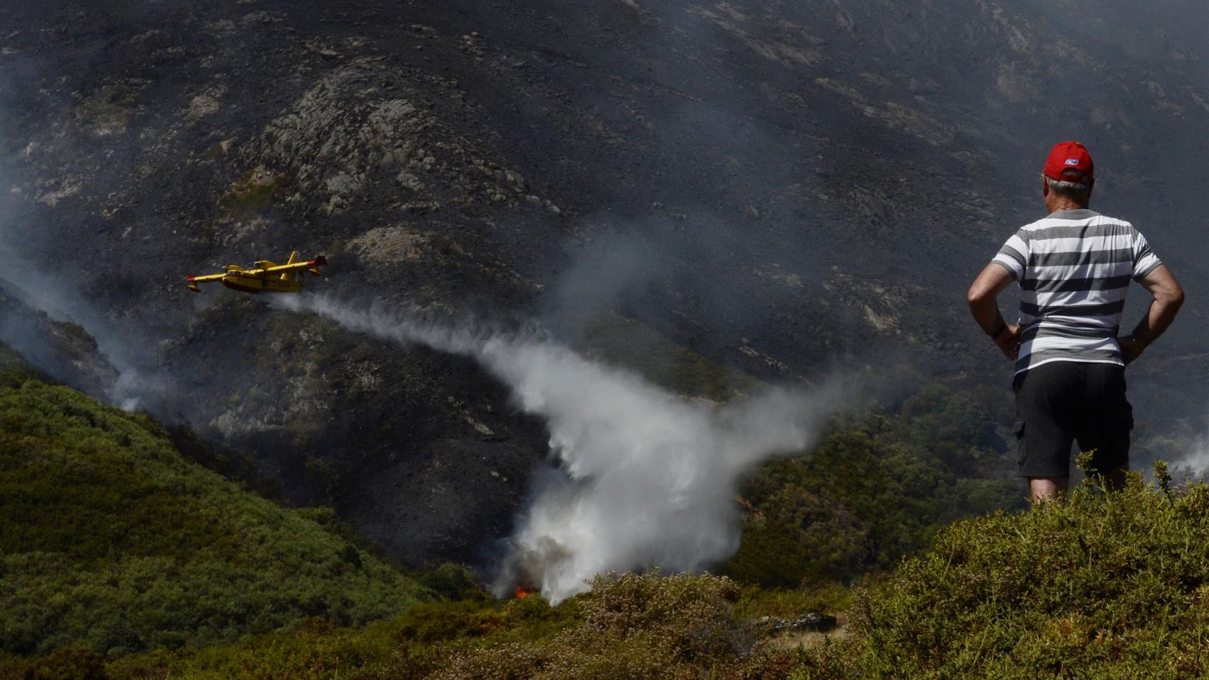 Un vecino de Senderiz en Lobeira observa un hidroavión trabajar en el incendio forestal en la Serra do Leboreiro, en el parque natural de Baixa Limia e Serra do Xurés.