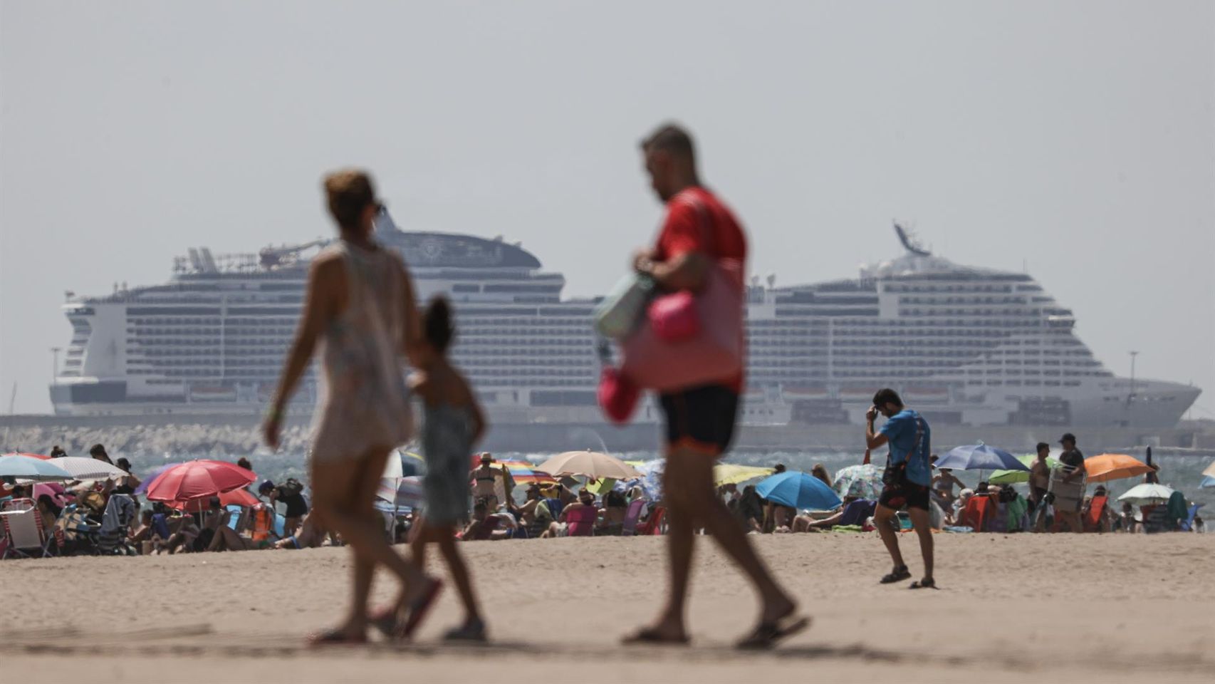 Varios turistas en una playa valenciana con varios cruceros de fondo, este verano.