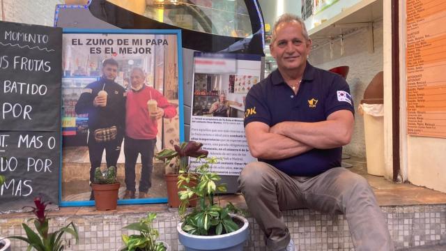 Ismael, padre de Omar Montes, sentado en la puerta de su tienda donde sale en una foto con su hijo probando un zumo.
