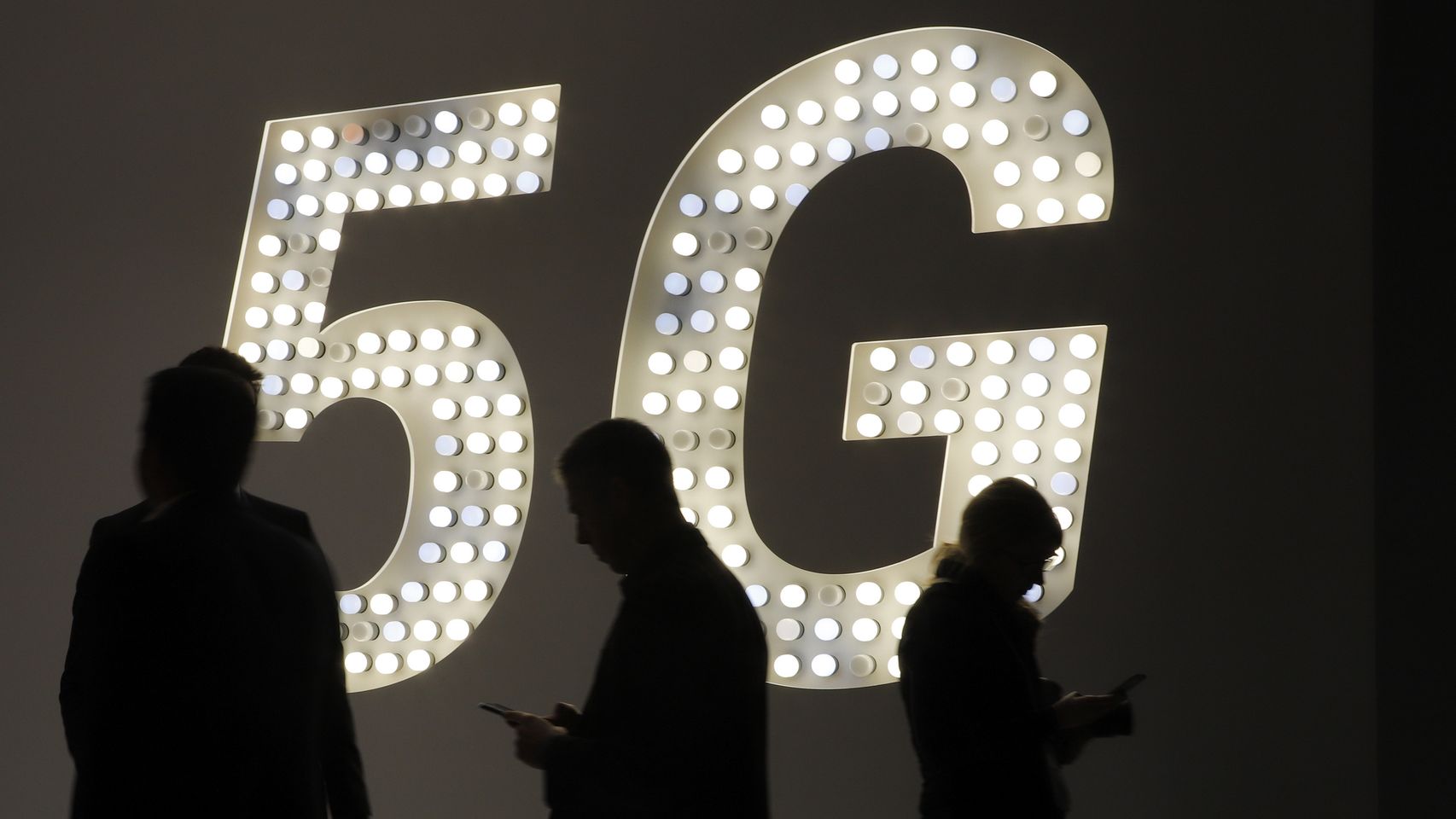 Varias personas mirando su teléfono móvil delante de un luminoso del 5G.