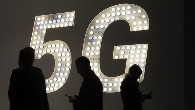 Varias personas mirando su teléfono móvil delante de un luminoso del 5G.
