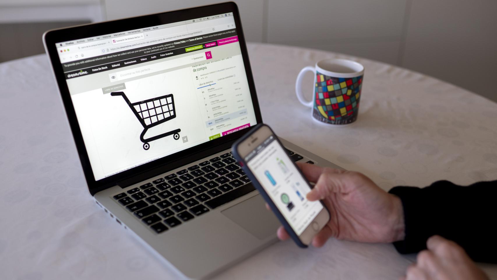 Una persona realizando compras online con su teléfono móvil y ordenador