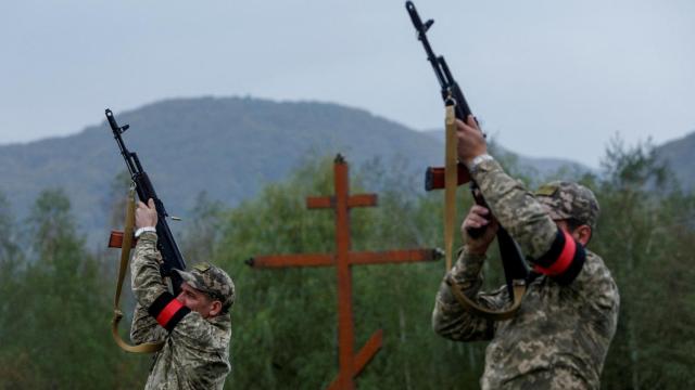 Dos soldados ucranianos homenajean a un compañero fallecido apuntando sus armas al aire.