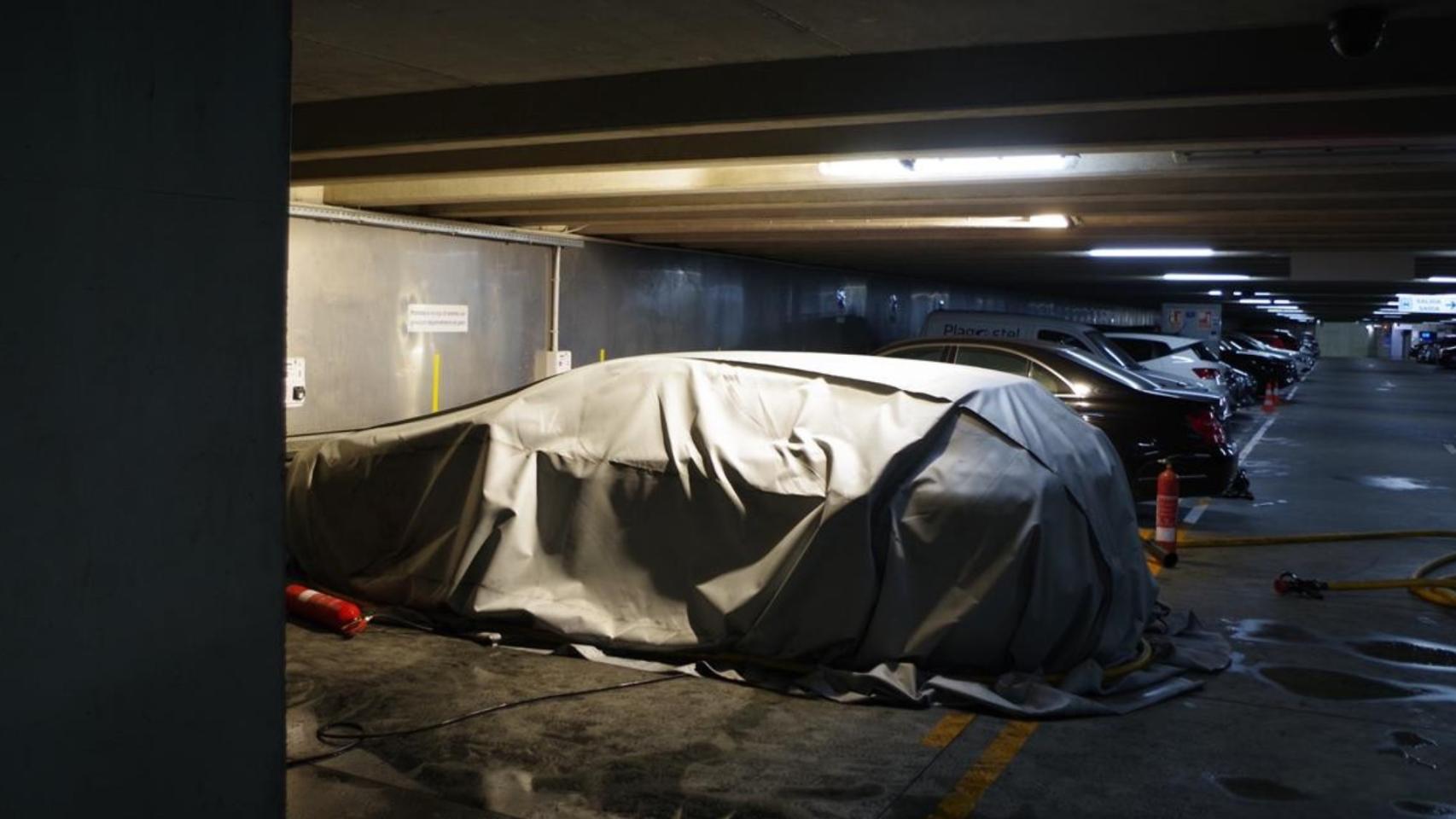 El coche tapado por una manta para tratar de apagar el fuego.