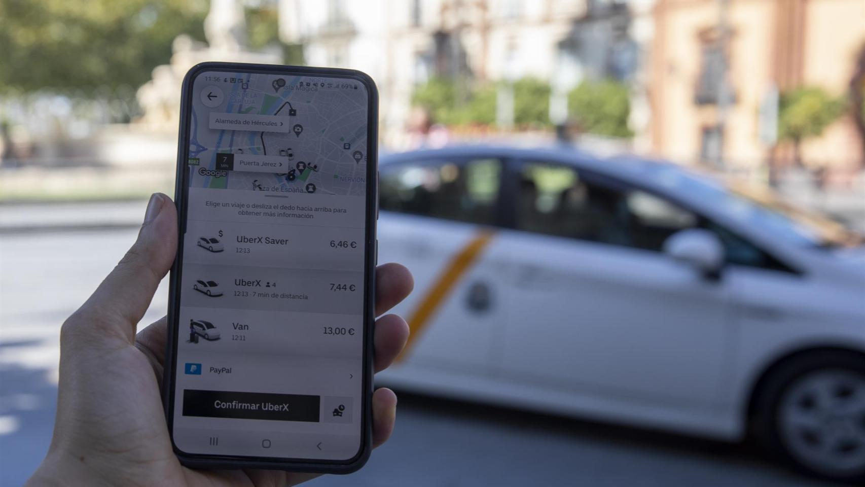 Imagen de un usuario con su teléfono móvil consultando los VTC ante una parada de taxis.