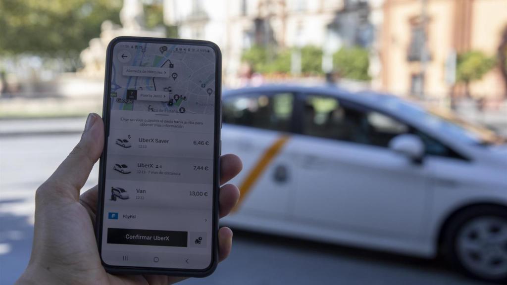 Imagen de un usuario con su teléfono móvil consultando los VTC ante una parada de taxis.