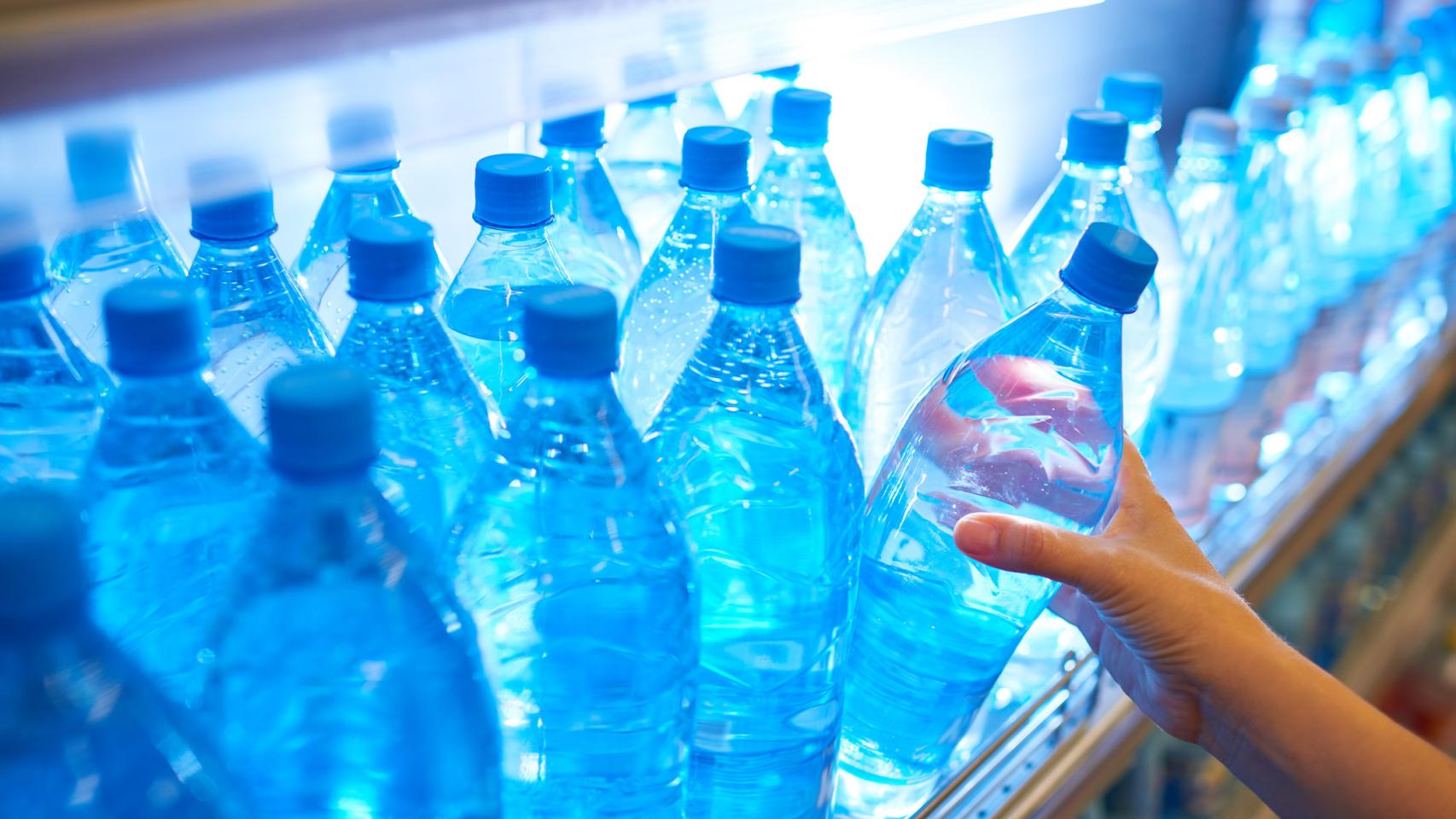Una joven cogiendo una botella de agua de un supermercado.