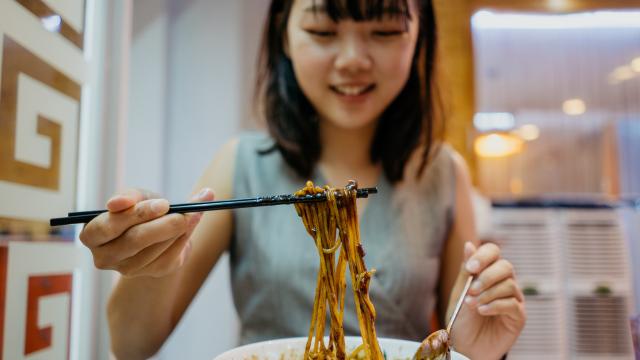 Una chica asiática comiendo con palillos.