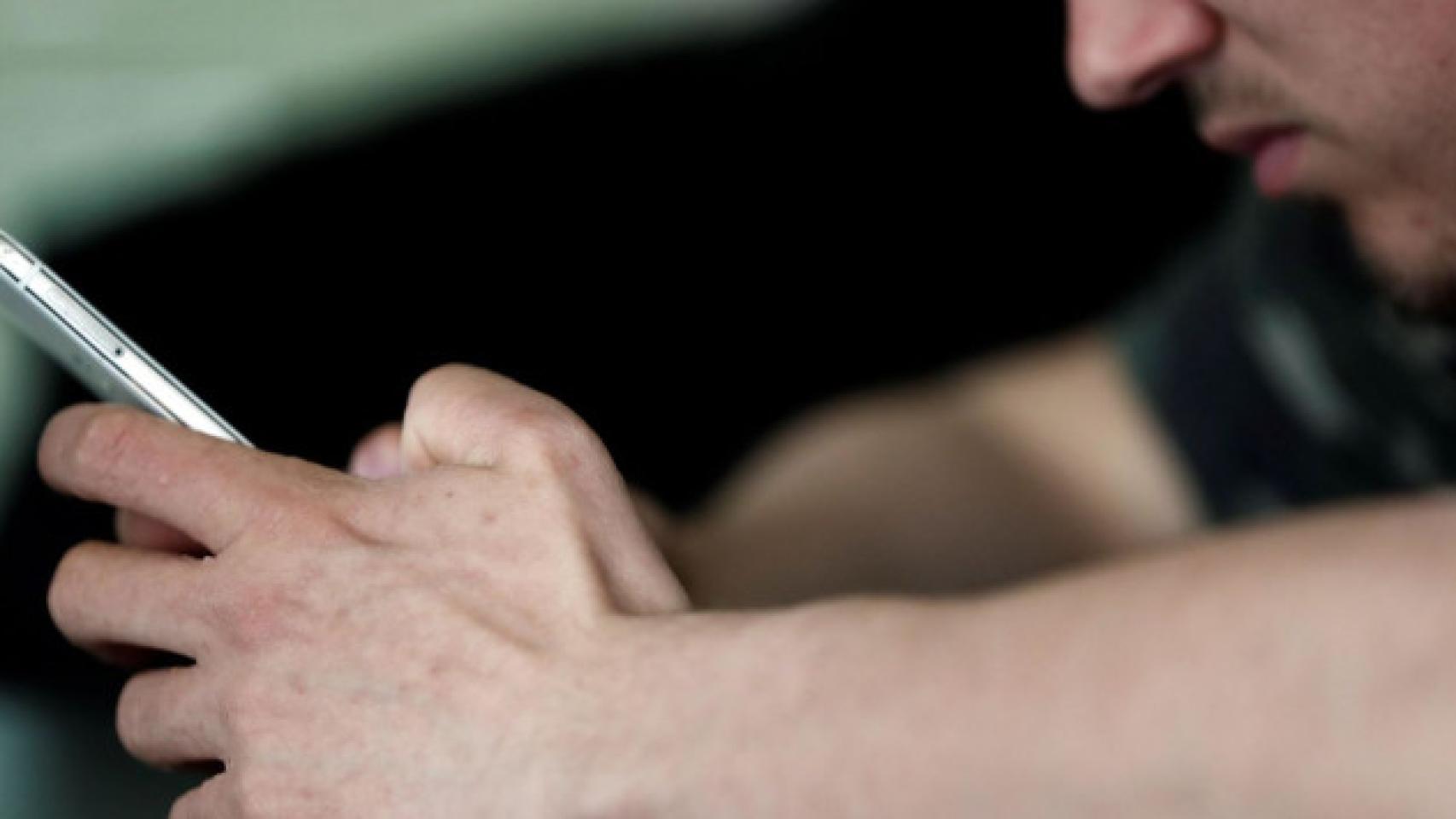 Un joven deprimido sujeta su móvil con la mano.